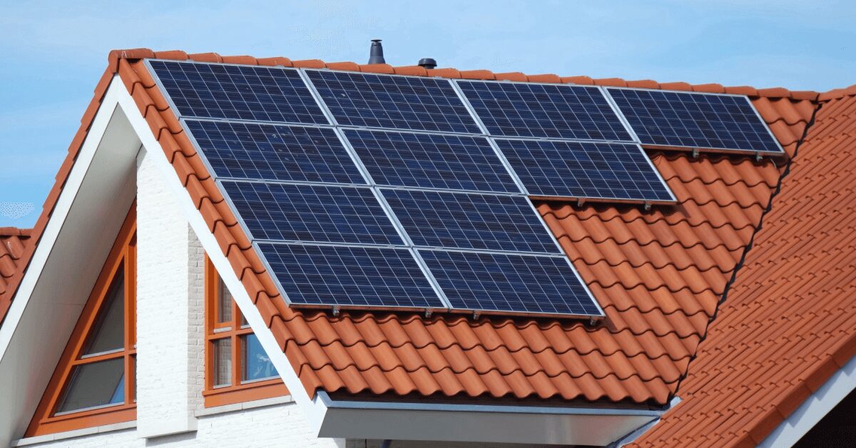 Solar panels mounted on a red-tiled pitched roof of a white house.