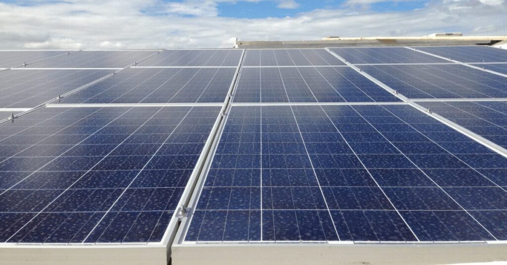Solar panels cover a flat roof, arranged in neat rows under a partly cloudy sky, harnessing solar energy.