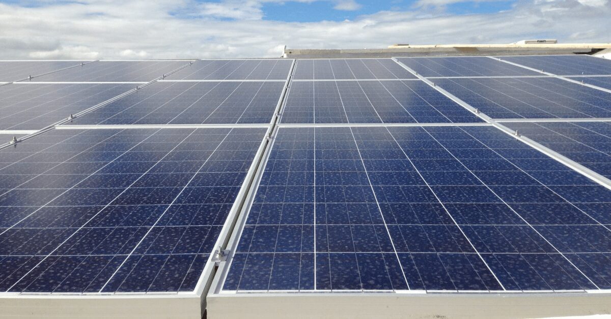 Solar panels cover a flat roof, arranged in neat rows under a partly cloudy sky, harnessing solar energy.