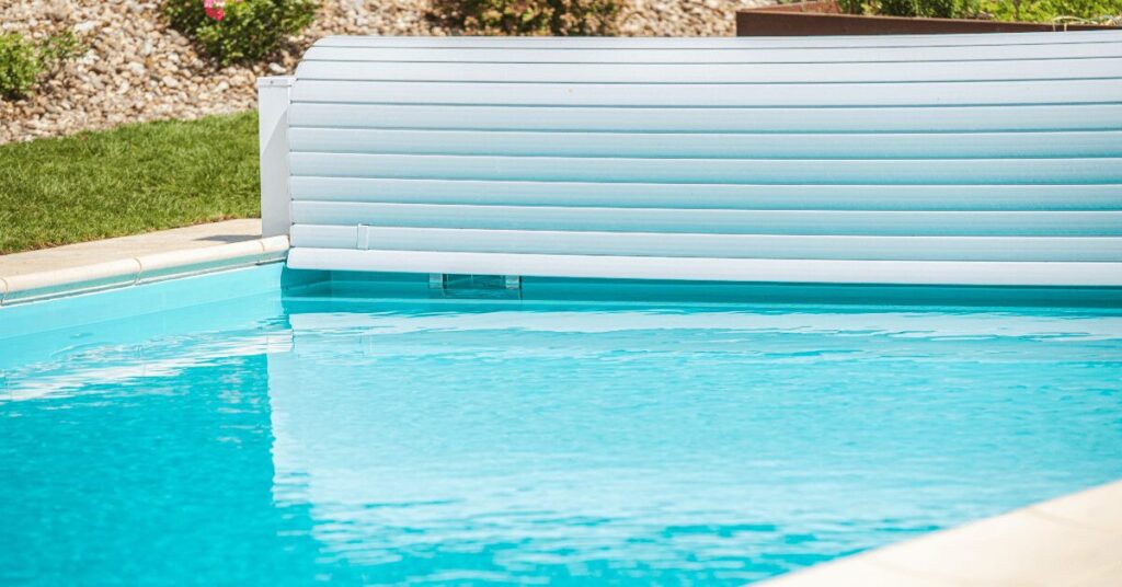 Swimming pool with a light blue rolled safety cover partially extended across the edge of the pool surface.