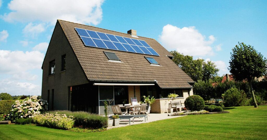 Residential house with solar panels on a sloped roof, outdoor dining on the patio, and a well-kept lawn under a blue sky.