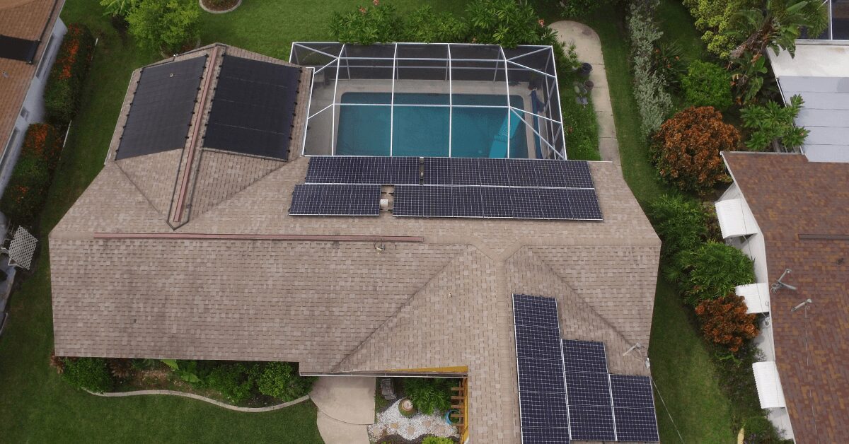 Aerial view of a house with solar panels on the roof and a fenced pool enclosure in the backyard.