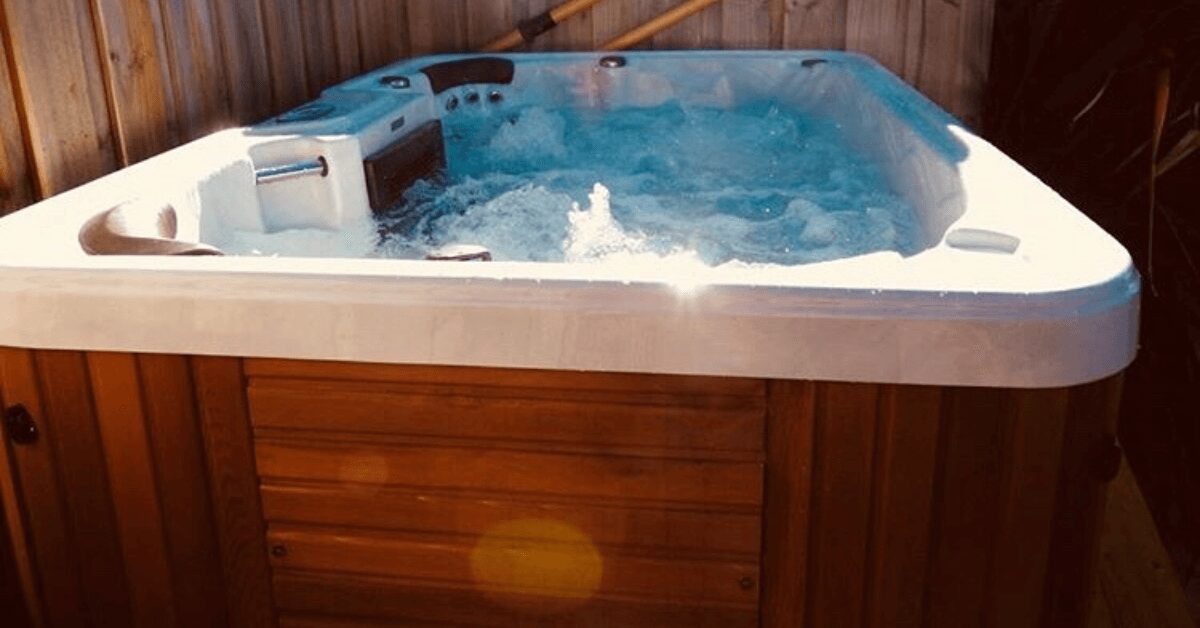 Outdoor white hot tub on a wooden deck, water bubbling with visible jets in a fenced area.
