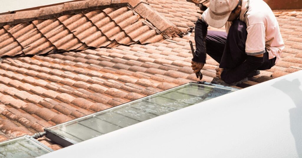 Roofer on a terracotta tiled roof installing a glass skylight window.