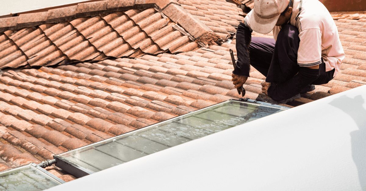 Roofer on a terracotta tiled roof installing a glass skylight window.