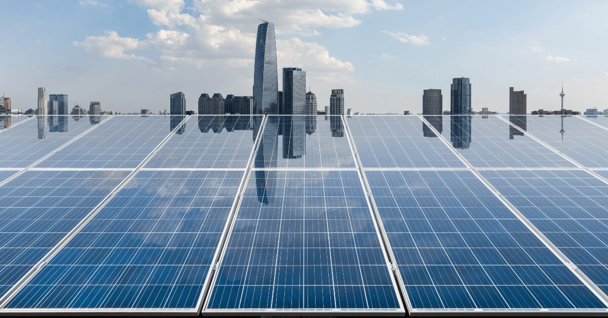 Rows of solar panels on a rooftop with a city skyline in the background.