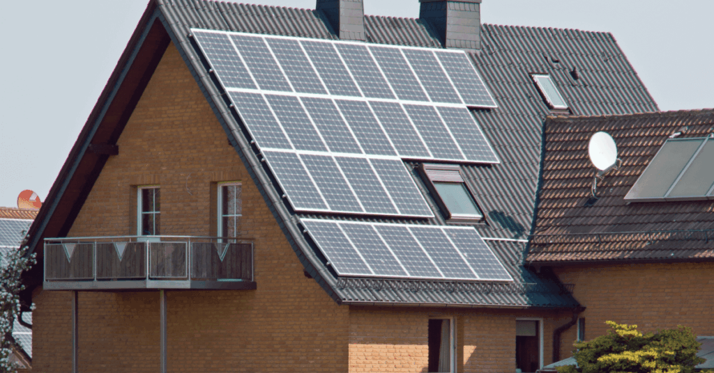 House with solar panels on a sloped roof, brick exterior, balcony, and satellite dish visible nearby.