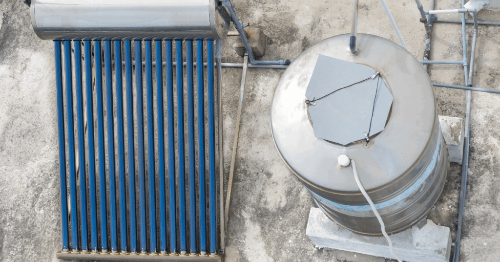 Overhead view of a rooftop solar water heating system with a row of blue-tube collectors next to a large metal storage tank and piping.