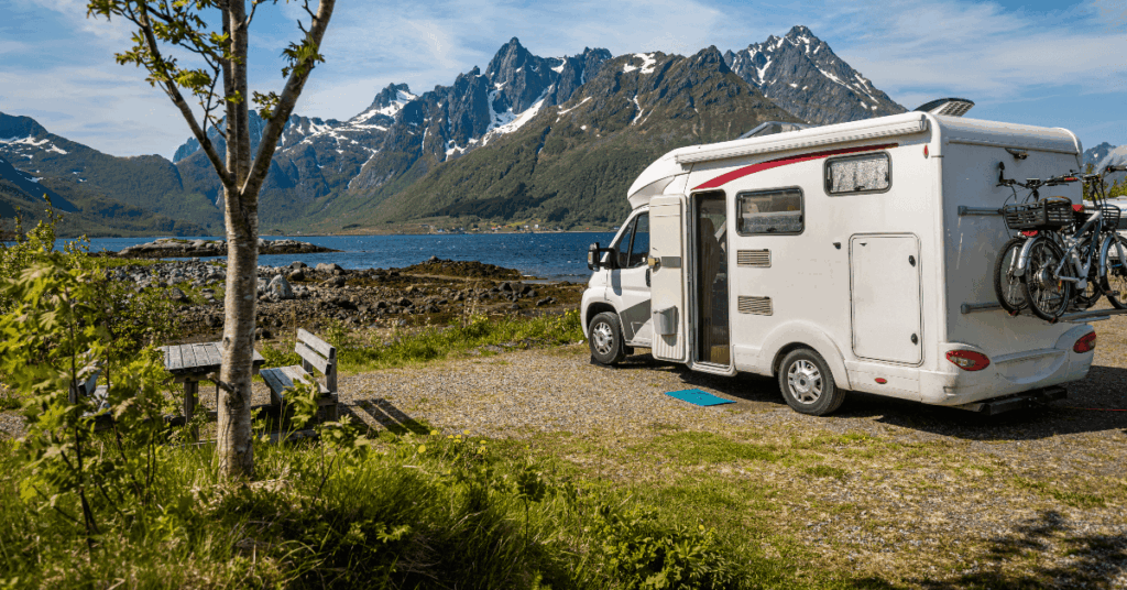 Camper van parked by a lakeside with snowy mountain peaks in the background and bikes on the rear rack.