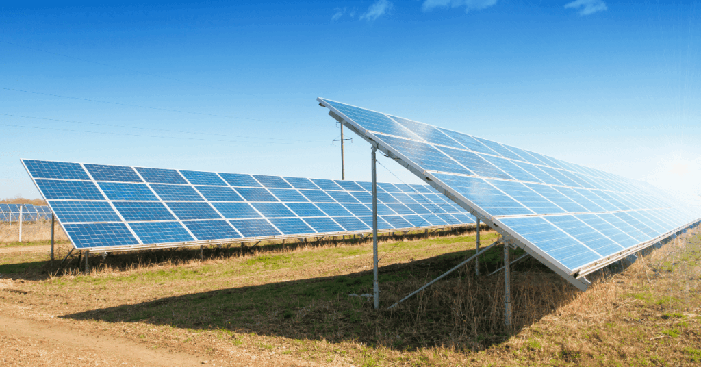 Solar farm with angled photovoltaic panels in a sunlit field under a clear blue sky.