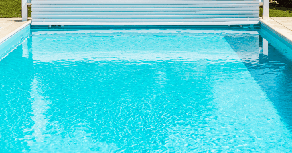 Blue swimming pool with a white pool cover rolled up at the far end, under a sunny sky.