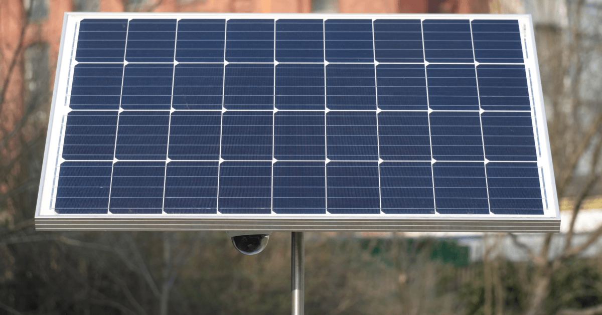 Outdoor solar panel mounted on a metal pole with a small, round sensor beneath it.