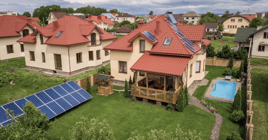 Suburban backyard with beige house and red tiled roof, solar panels on the main roof and a large ground-mounted solar array in the lawn.