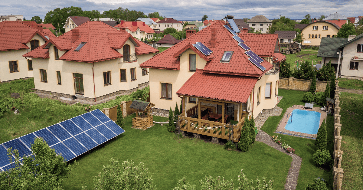 Suburban backyard with beige house and red tiled roof, solar panels on the main roof and a large ground-mounted solar array in the lawn.