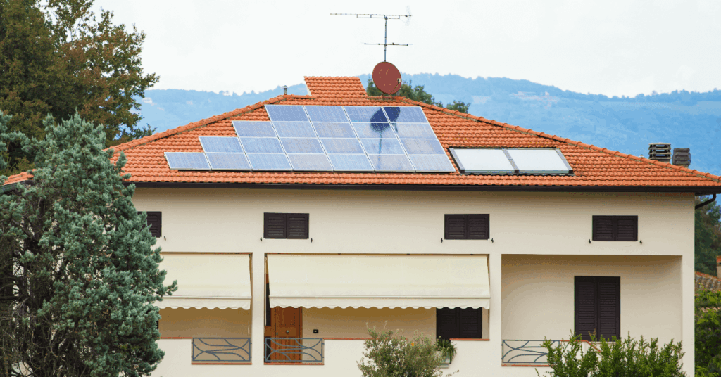 Residential house with solar panels on a red-tiled roof and a satellite dish in a mountainous backdrop.