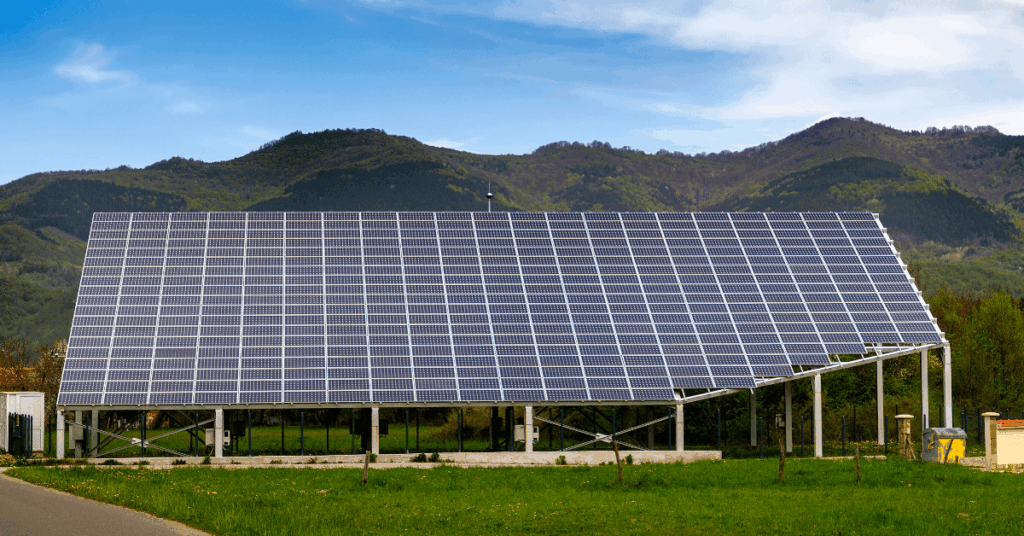 Ground-mounted solar farm with many rows of photovoltaic panels in a grassy field and hills in the distance.