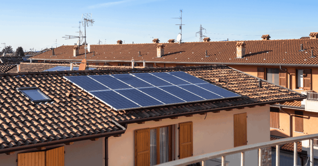 Residential rooftop with a large solar panel array on terracotta tiles under a clear blue sky.