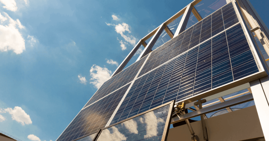 Solar panels mounted on a metal frame, angled on a building against a bright blue sky with a few clouds.