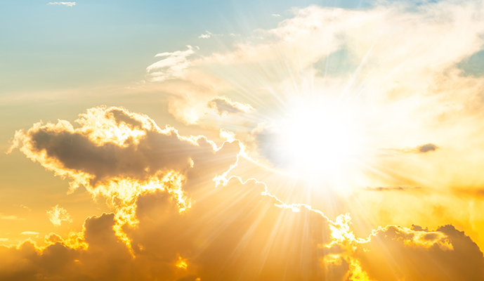 Bright sunburst breaking through golden clouds at sunrise/sunset with radiating light beams away from the sun.