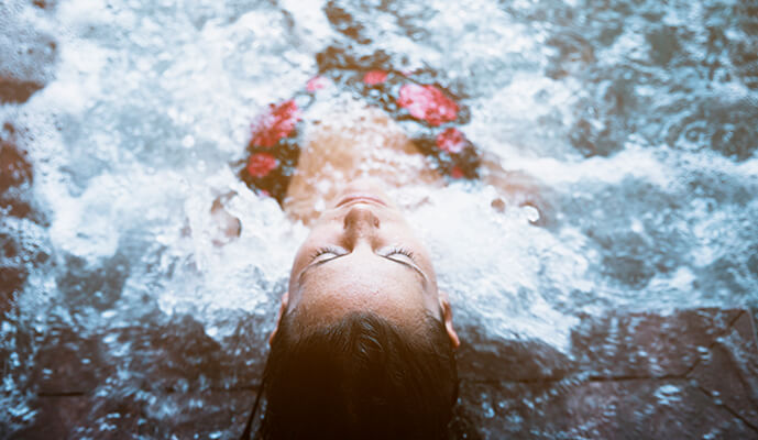 Top-down view of a person floating face-up in a pool, water rippling around them.
