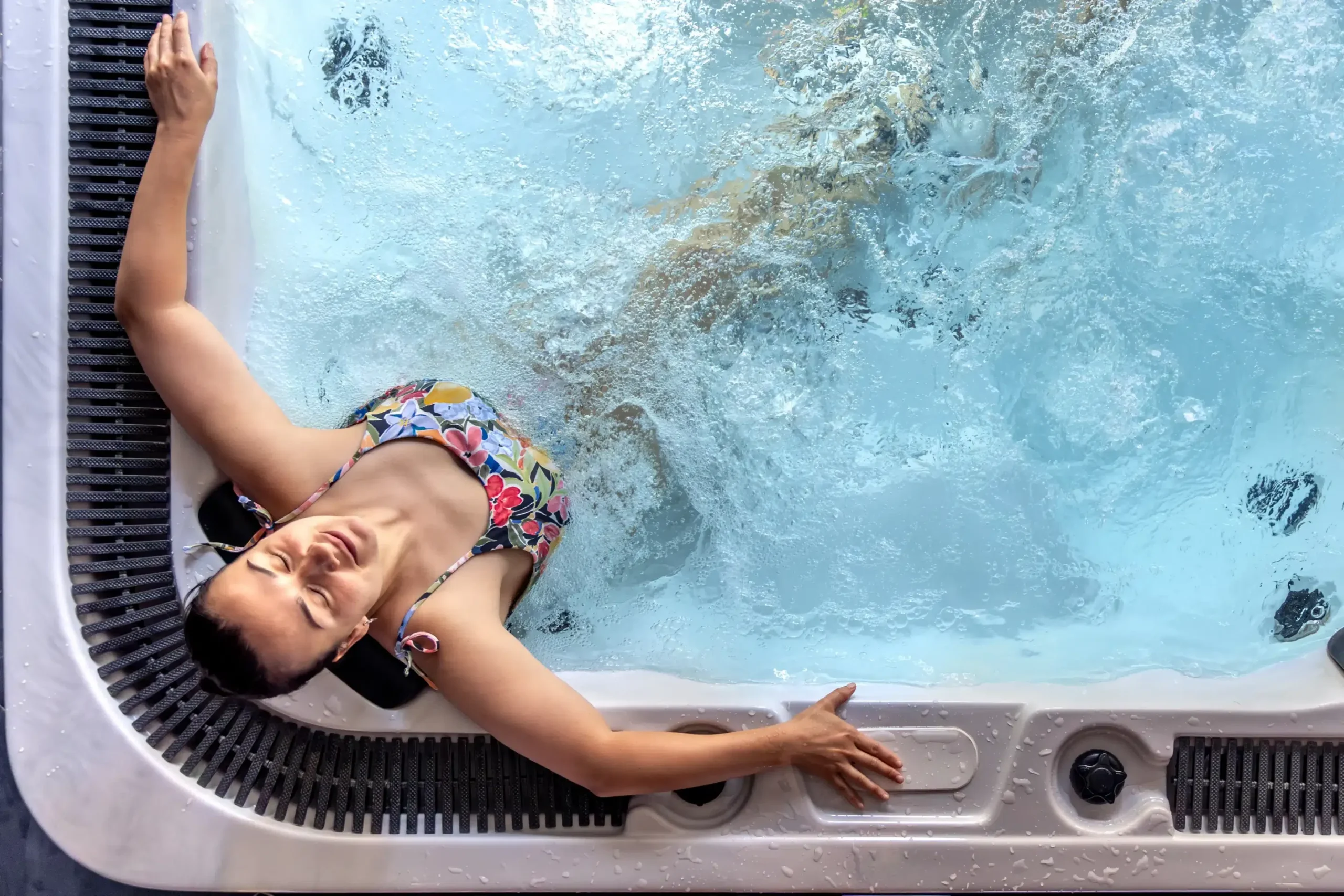 Woman in a floral bikini relaxing in a bubbly hot tub, resting her arms on the edge.
