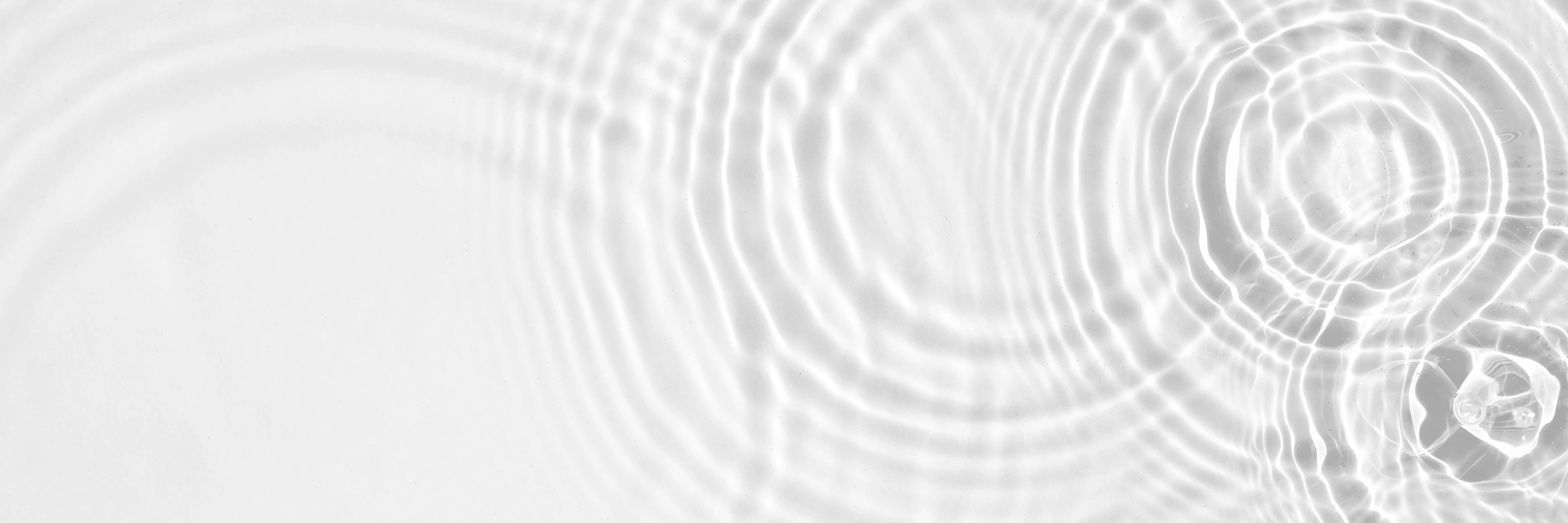 Monochrome close-up of ripple patterns on a bright surface, with a clear glass object visible in the right edge.