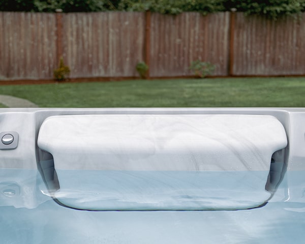 White hot tub cover partially opened, with blue water visible, set in a backyard with a wooden fence and green lawn.