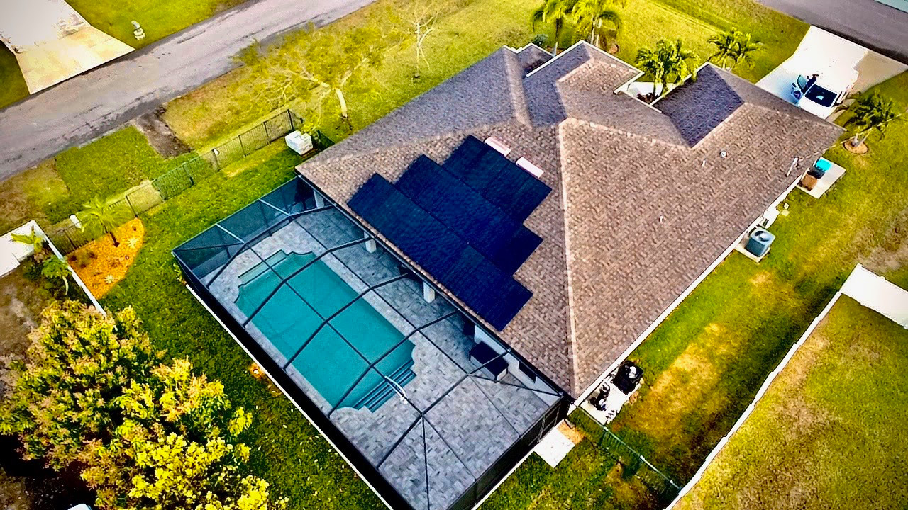 Aerial view of a house with a screened-in rectangular pool and solar panels on the roof on a sunny day.