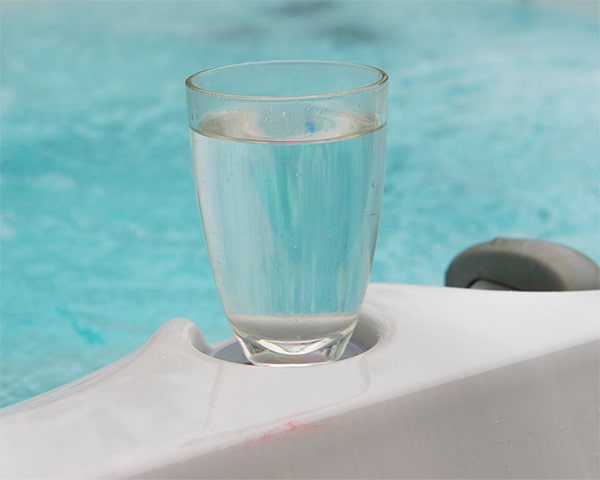 Glass of water resting on the white pool edge with blue pool water in the background.