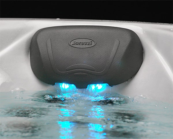 Black hot tub control unit mounted on the tub wall with two blue LED-lit jets visible in the water below.