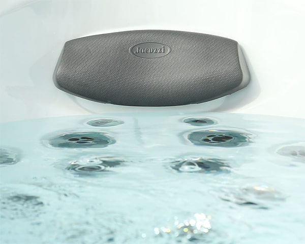 Black textured Jacuzzi speaker mounted on the edge of a white soaking tub, with several water jets visible in the water.