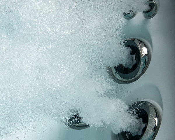 Chrome hot tub jets releasing bubbles in a spa tub. (close-up)