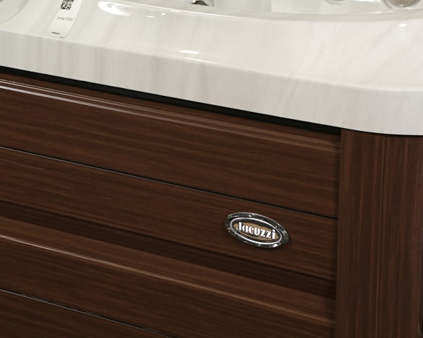 Close-up of a dark wood bathroom vanity with a marble top and a chrome oval badge reading 'RIGUZZI' on the drawer panel.