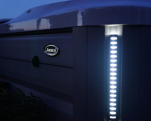 Outdoor Jacuzzi hot tub at dusk with a bright vertical LED light strip along the side.