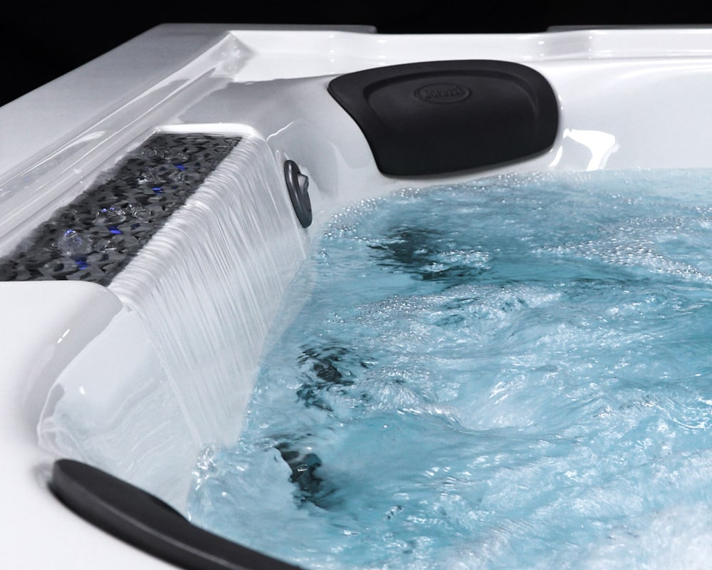 White hot tub with a cascading waterfall edge, a black backrest, and blue bubbling water.