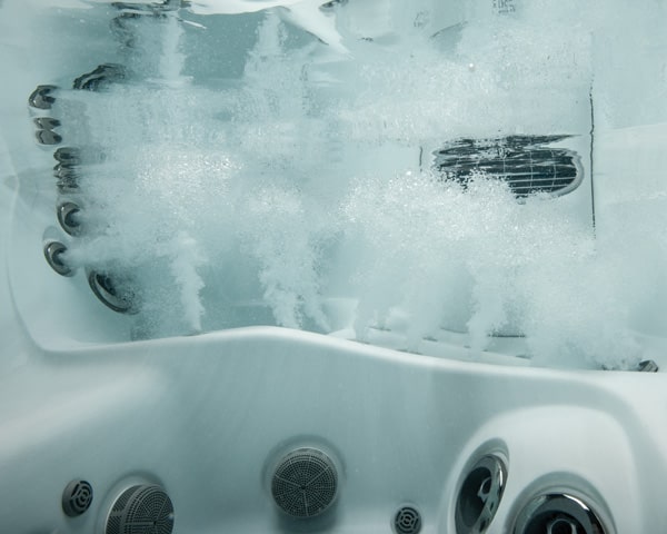 White hot tub with bubbling water and multiple circular jets along the edge.