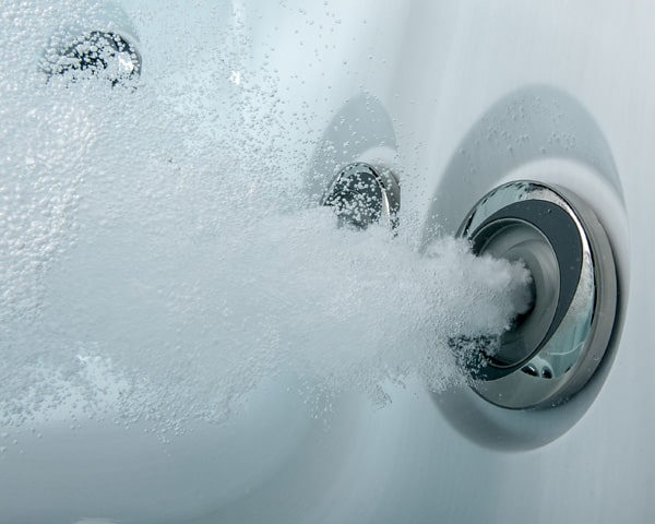 Close-up of a modern chrome shower faucet spraying water into a tub.