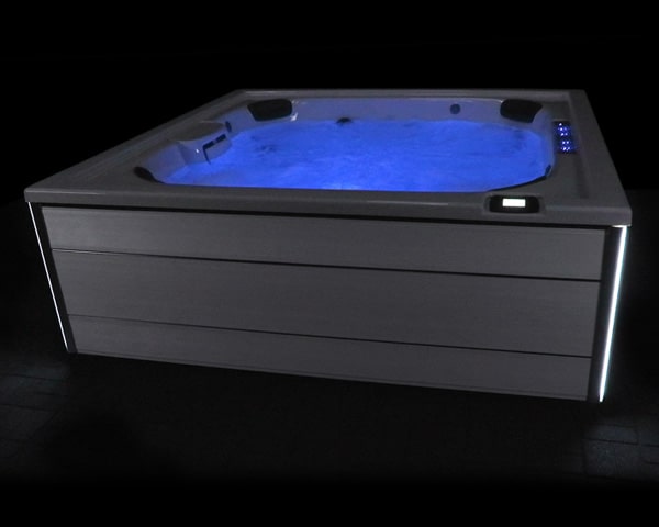 Rectangular modern hot tub with blue underwater lighting, built-in jets, and edge lighting in a dark setting