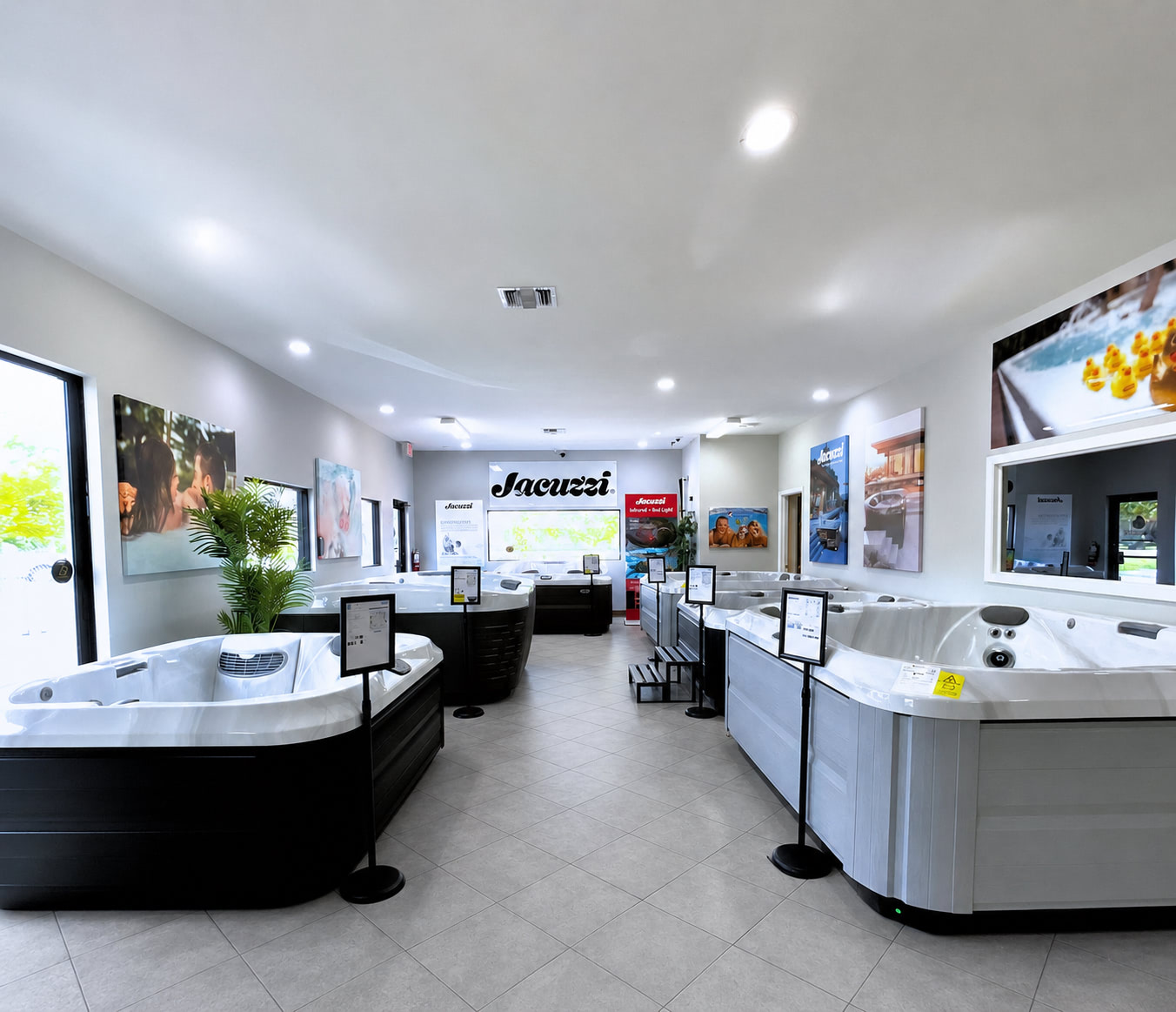 Showroom with multiple white and black hot tubs, promotional posters, and a large Jacuzzi sign on the back wall.