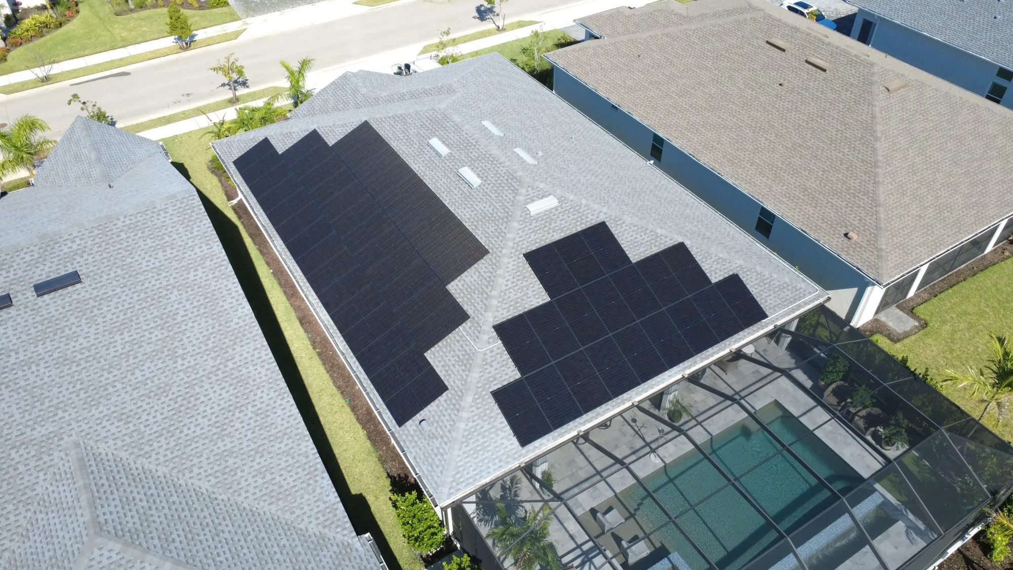 Aerial view of suburban houses with solar panels on gray roofs and green lawns nearby streets.