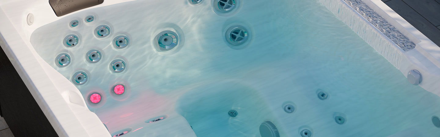 White hot tub filled with water, dozens of circular jets along the seats and pink LED lights glowing underwater.