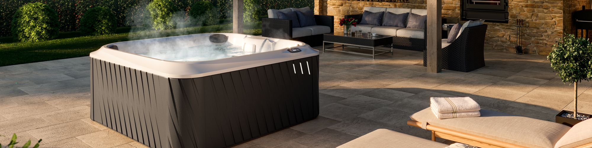 Outdoor patio scene featuring a steaming hot tub beside a wicker seating area and a stone fireplace. The space feels luxurious and inviting.