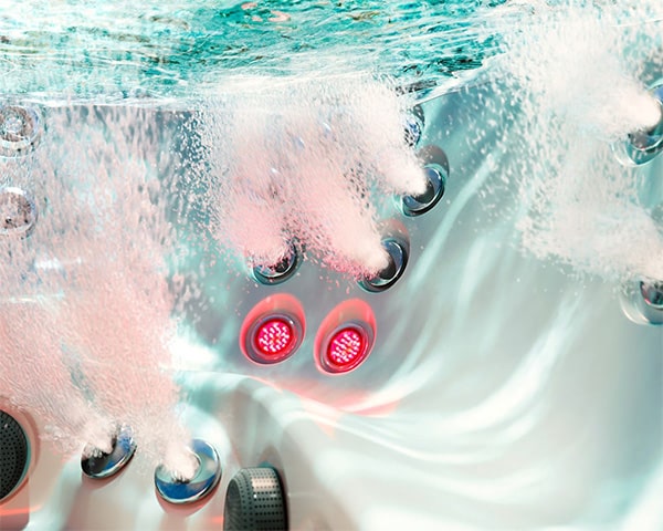 Underwater view inside a modern hot tub with red LED jet lights and rising bubbles.