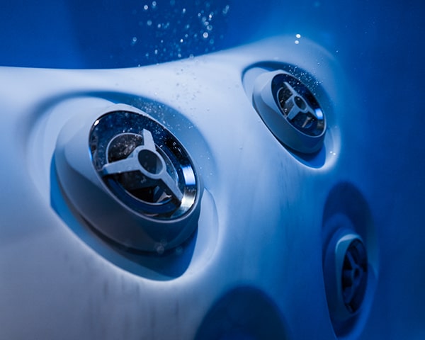 Close-up of circular spa jets embedded in a white hot tub, lit in blue tones.