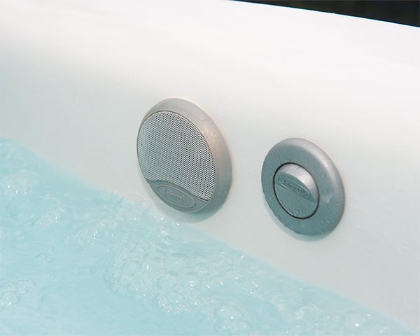 Close-up of two round metallic spa jets mounted on a white hot tub wall above turquoise bubbling water.