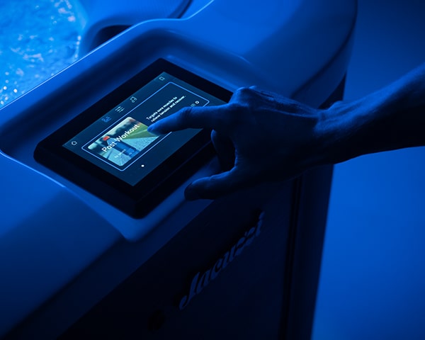 Person uses a blue-lit touchscreen control panel on a hot tub/jacuzzi, selecting settings with a finger.