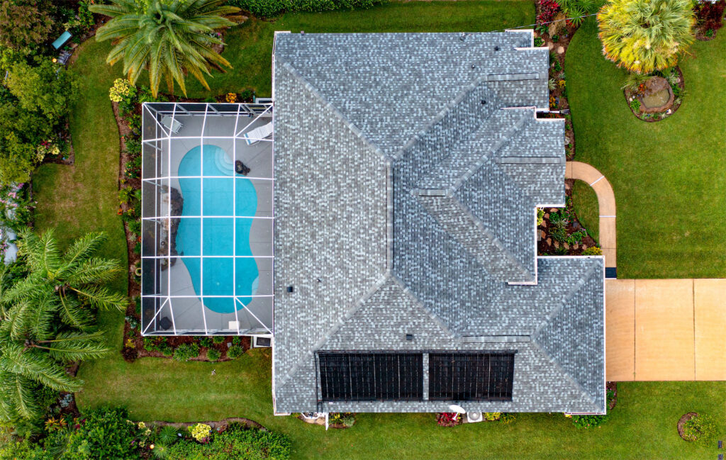 Aerial view of a gray-roofed house with a screened-in pool enclosure on the left and landscaped green lawn surrounding it.