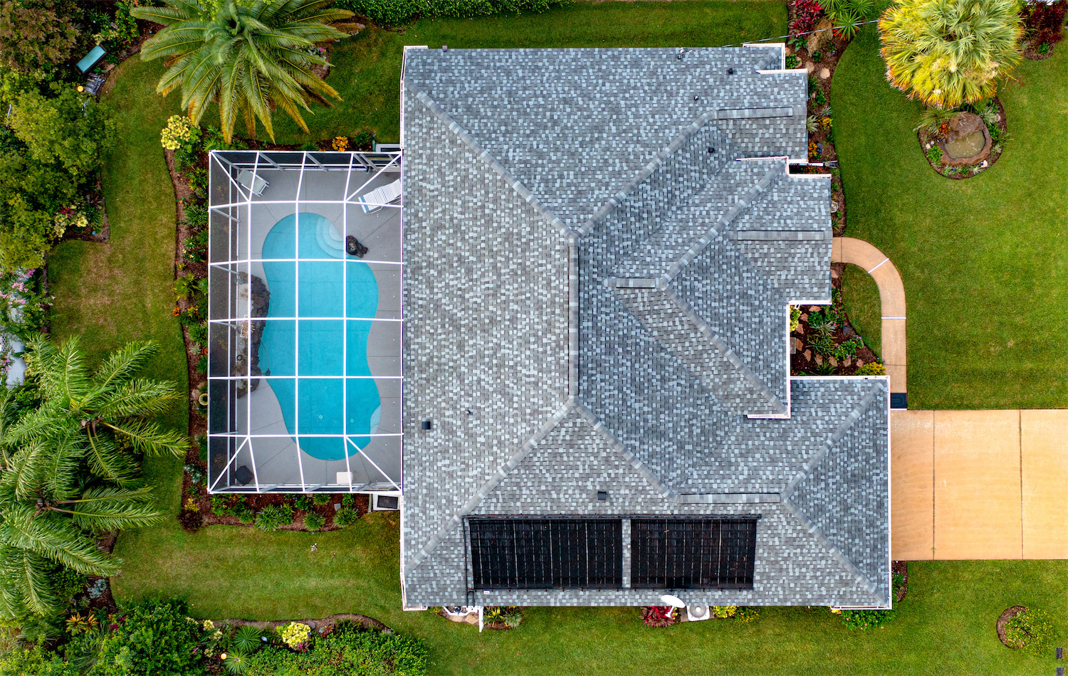 Aerial view of a gray-roofed house with a screened-in pool enclosure on the left and landscaped green lawn surrounding it.